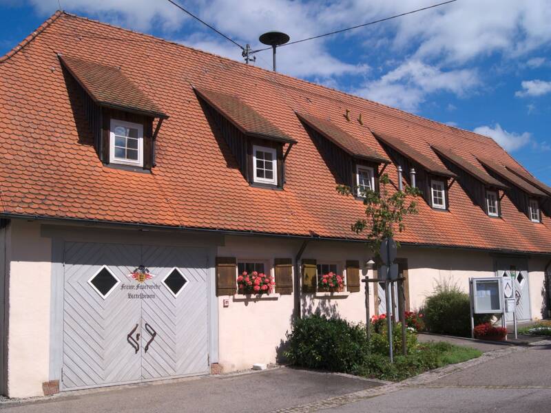 Ein traditionelles, weißes Fachwerkhaus mit niedrigem, rotem Satteldach und kleinen Dachfenstern, umgeben von blauen Himmel und vereinzelten Wolken.